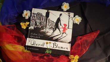 Buch "Überall Blumen" auf bunten Tüchern, drumherum einzelne Blüten