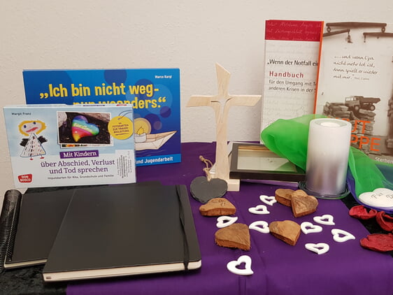 Tisch mit Holzkreuz, Kerze, Büchern, Kondolenzbüchern, Blütenblättern etc.