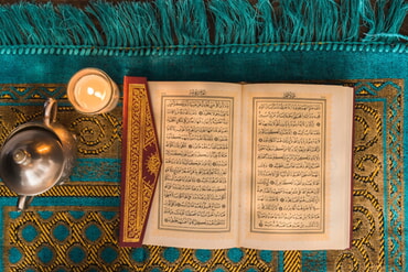 Kunstvoll verziertes Buch mit arabischer Schrift, Kerze und Metalldose auf orientalischem Teppich
