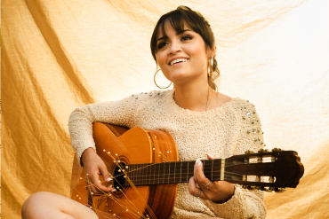 lächelnde Frau, die im Schneidersitz Gitarre spielt